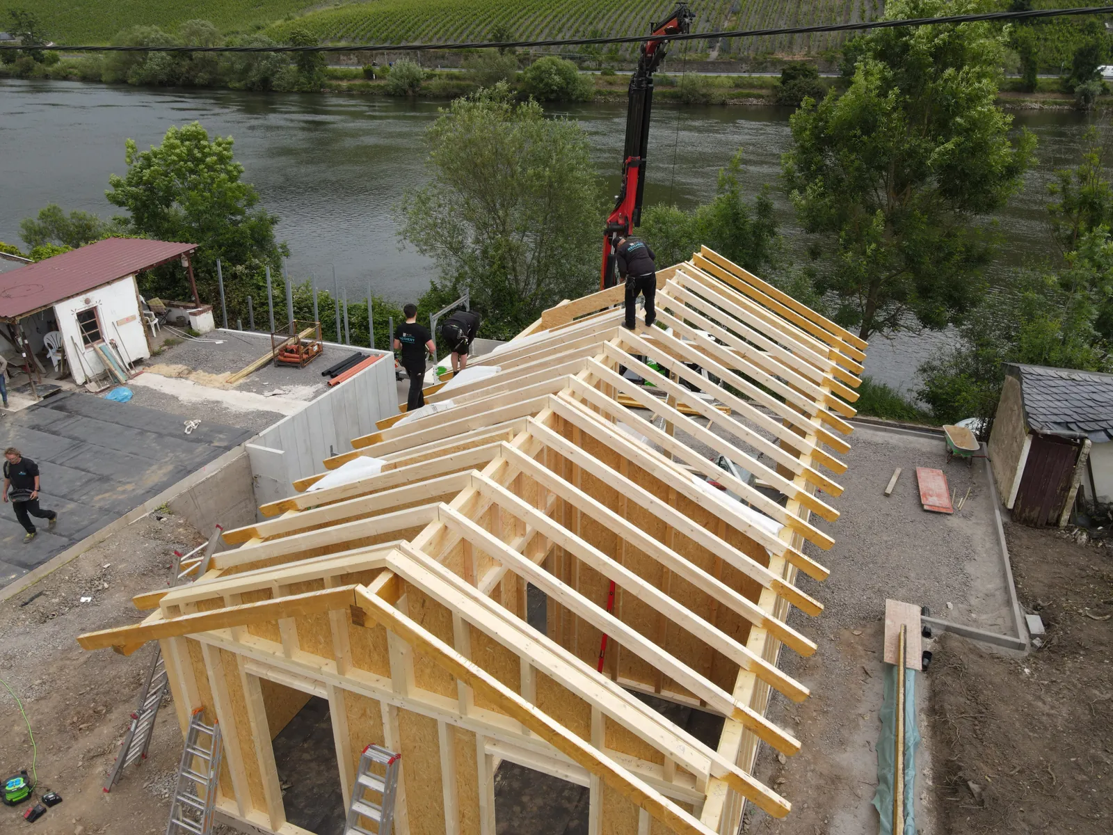 Drohnenaufnahme: Zimmerer von Reichert Holzbau richten einen neuen Dachstuhl aus Holz auf, im Hintergrund die Mosel