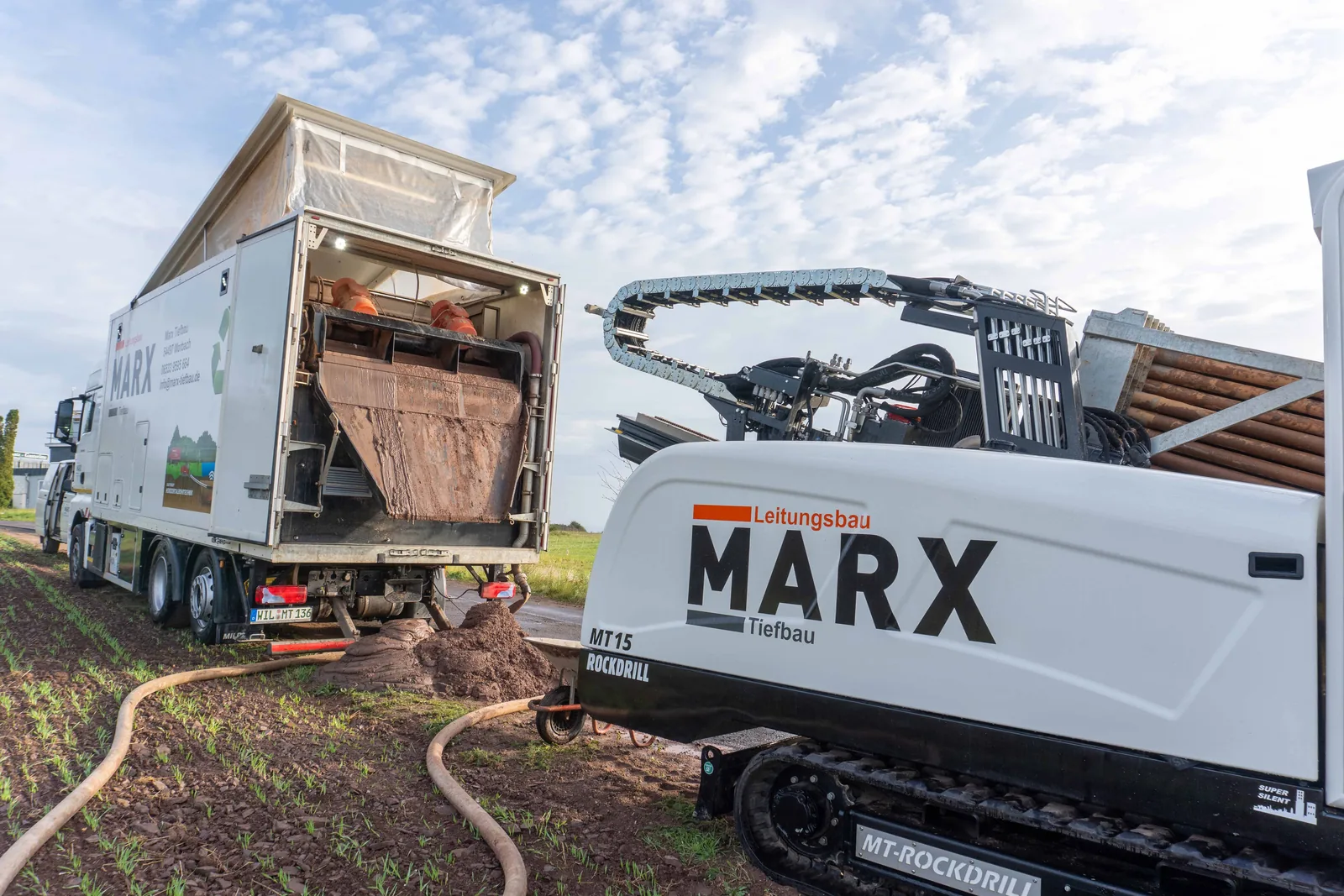 Horizontalbohrgerät und Lkw von MARX Tiefbau auf einer Baustelle neben einem Feld