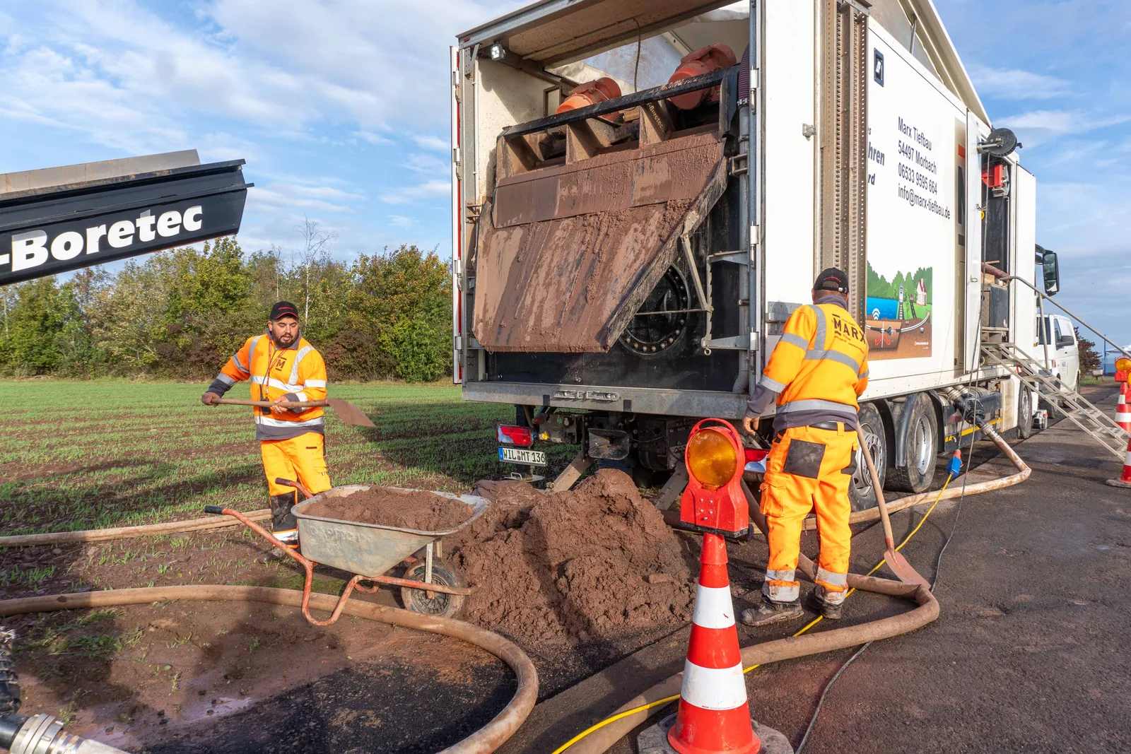 Mitarbeiter von MARX Tiefbau arbeiten an einem Bohrfahrzeug auf einer Baustelle am Straßenrand