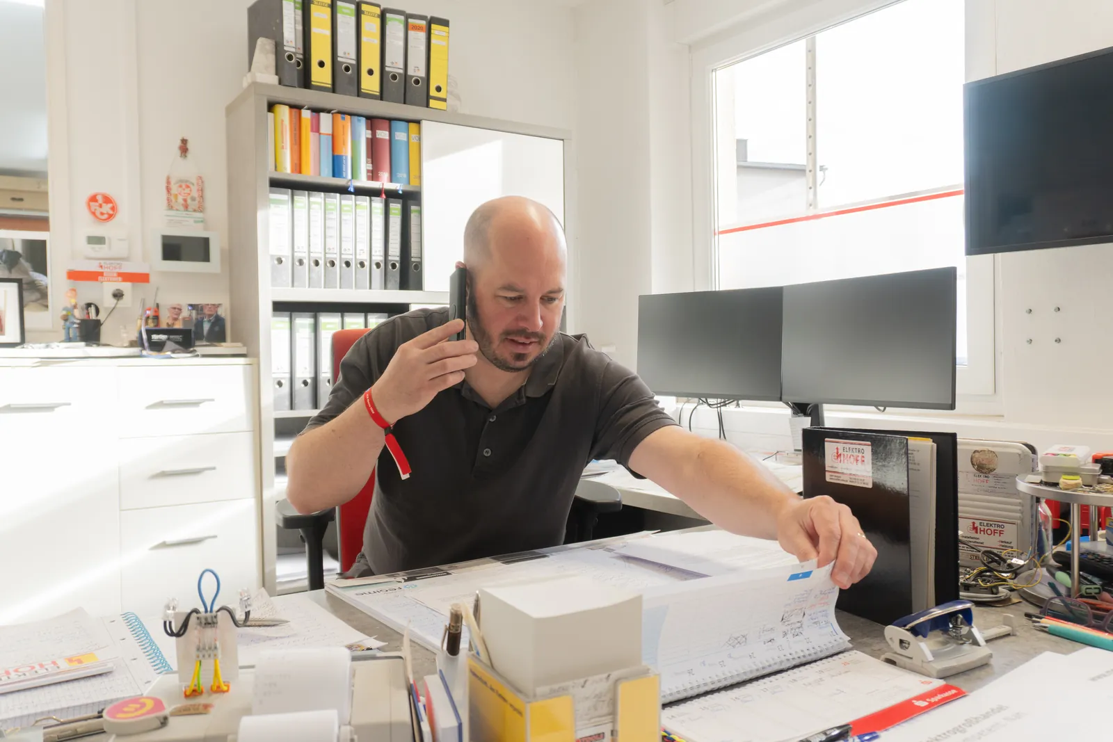Mitarbeiter von Elektro Hoff telefoniert am Schreibtisch im Büro und blättert in Unterlagen