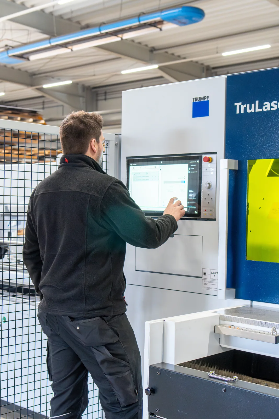 Mitarbeiter bedient das Bedienfeld einer großen Laserschneidanlage bei Hand in Hand Industriemontage