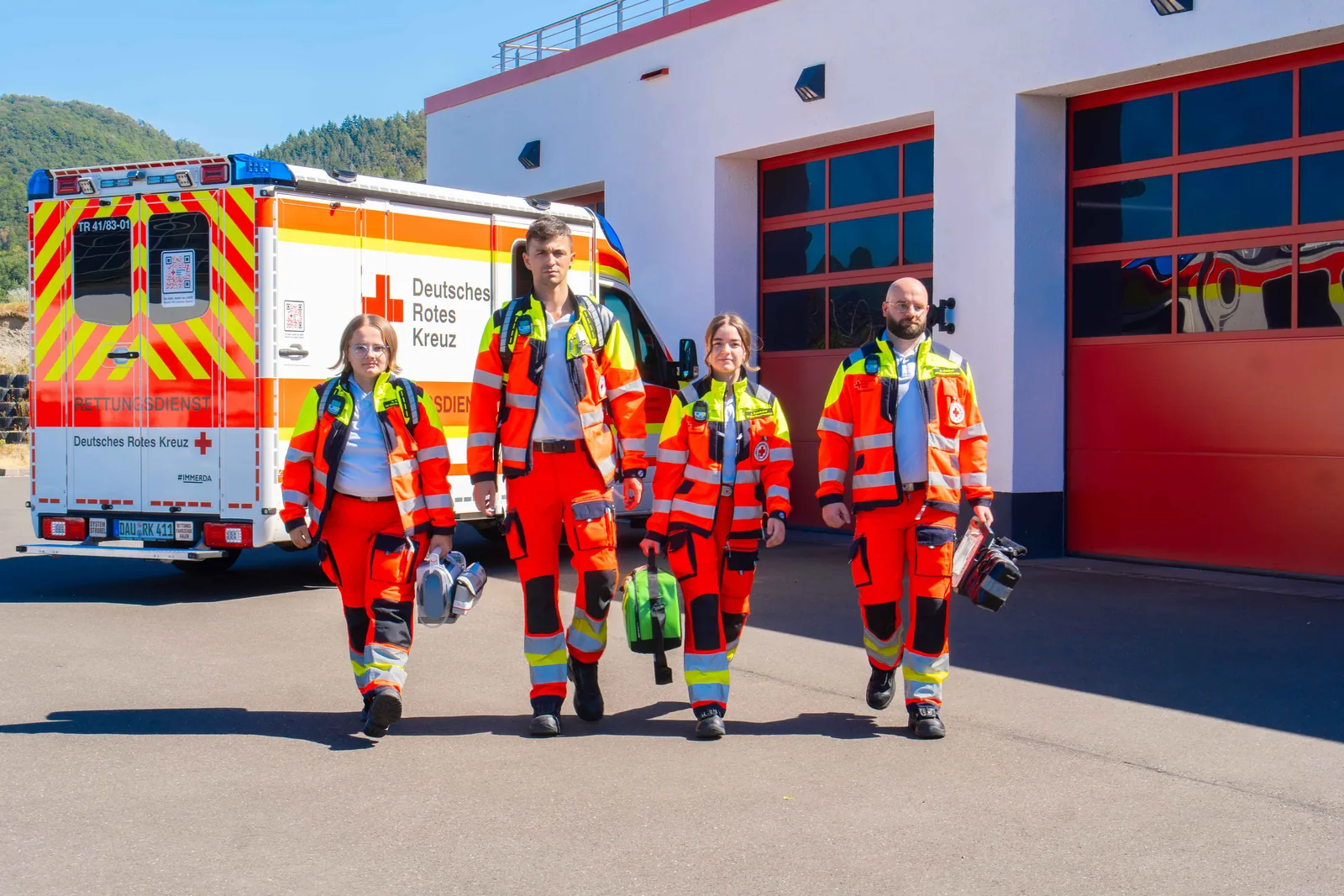 Vier Notfallsanitäter des DRK gehen in Einsatzkleidung über den Hof der Rettungswache