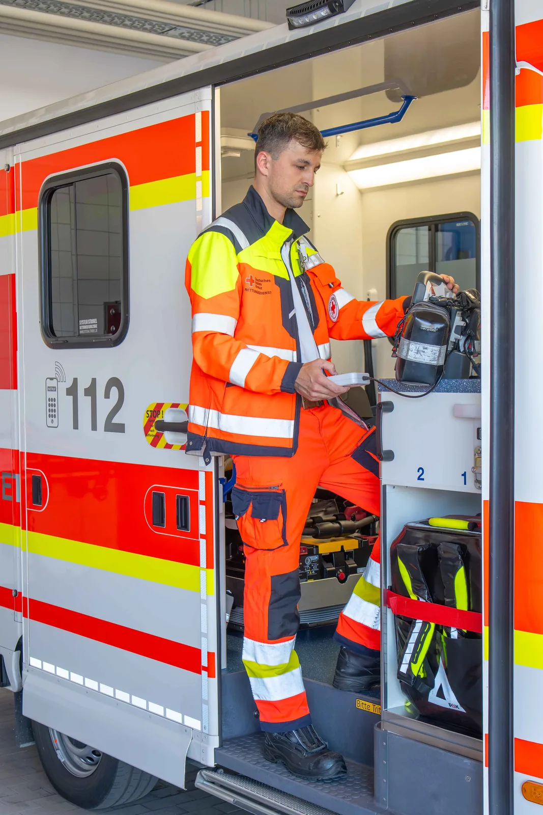 Notfallsanitäter steht in der offenen Seitentür eines DRK Rettungswagens und prüft die Ausrüstung