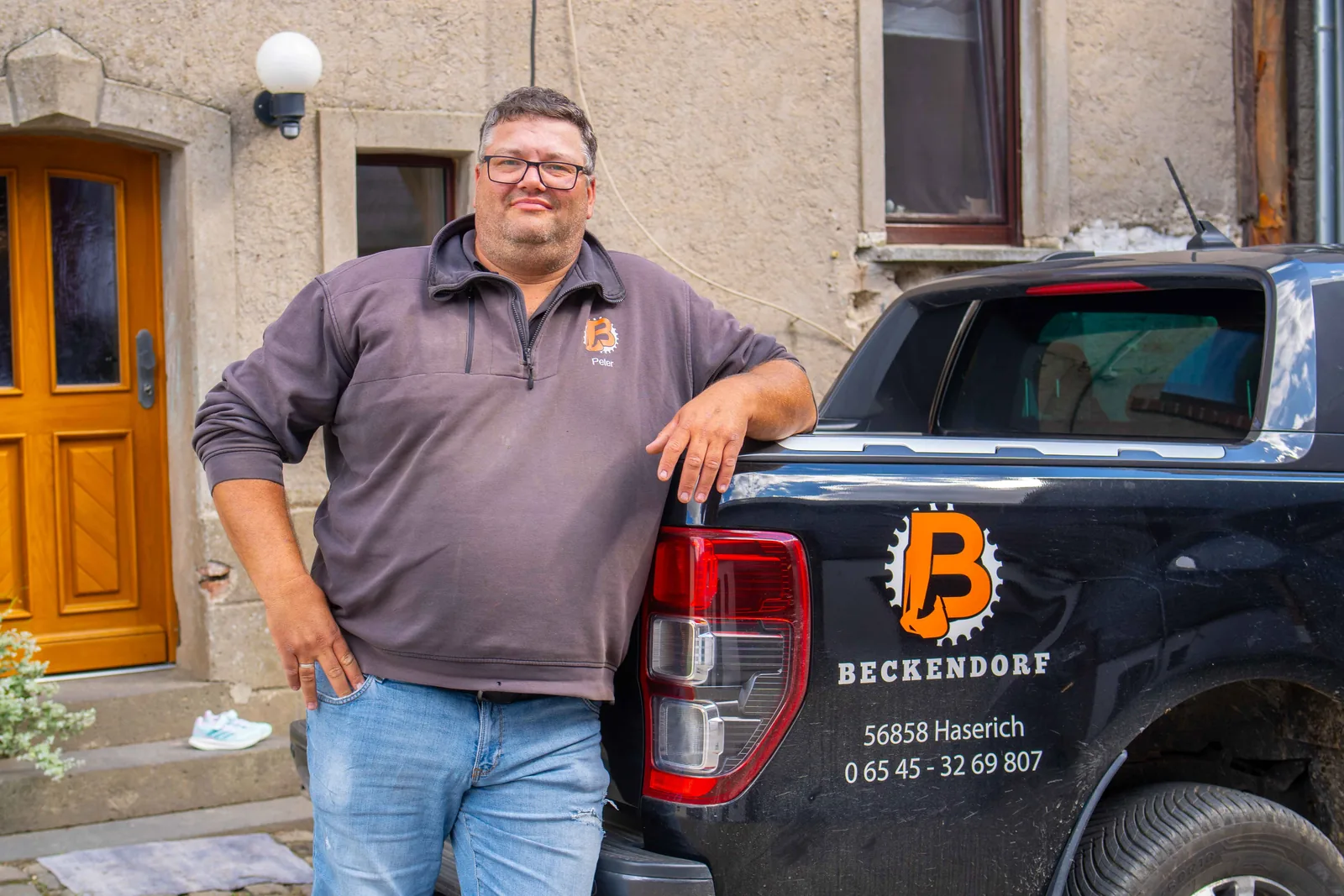 Mitarbeiter der Beckendorf GmbH lehnt lächelnd an einem Pick-up mit Firmenlogo