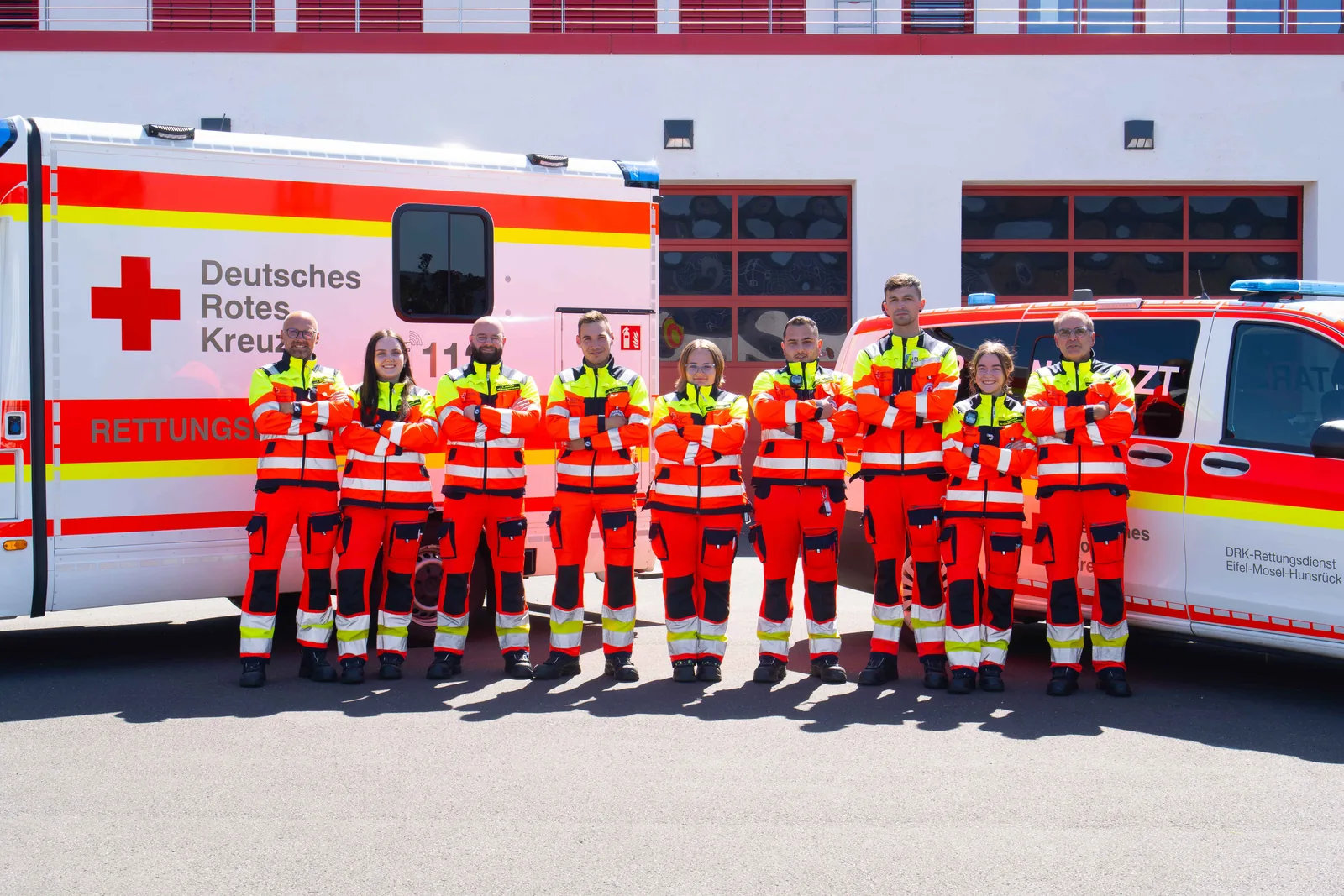 Team des DRK Rettungsdienstes in Einsatzkleidung steht vor Rettungswagen an der Rettungswache
