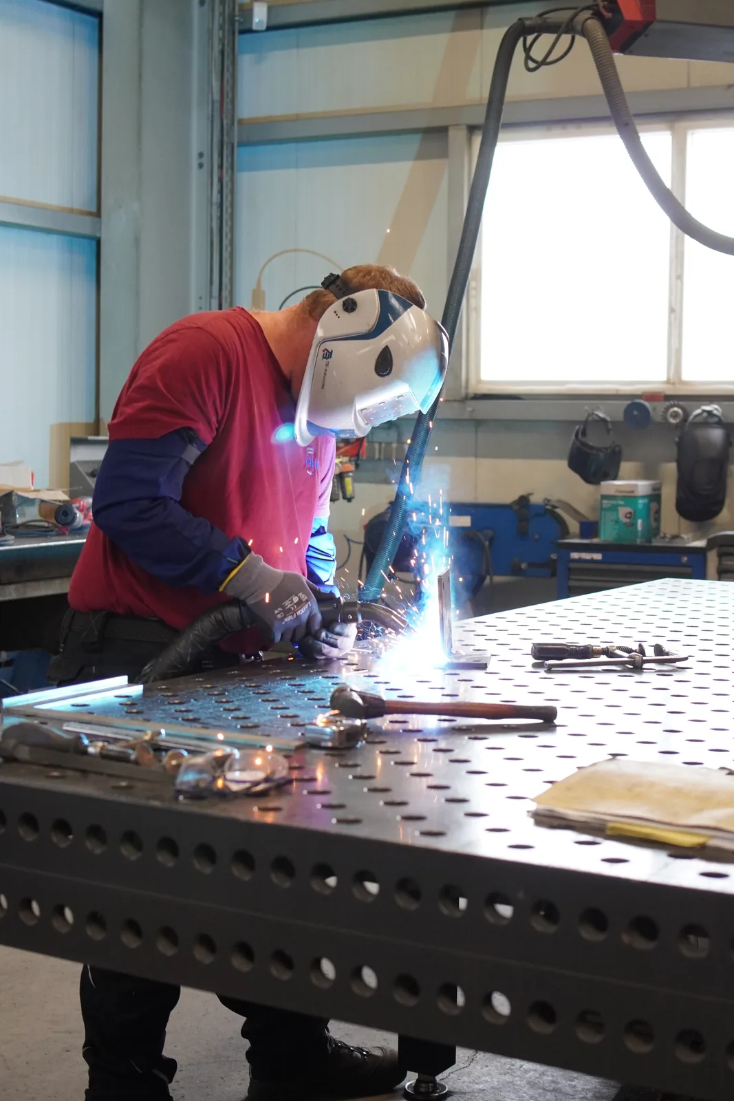Schweißer mit Schutzhelm schweißt an einem Werktisch, Funken sprühen in der Halle von Hand in Hand Industriemontage