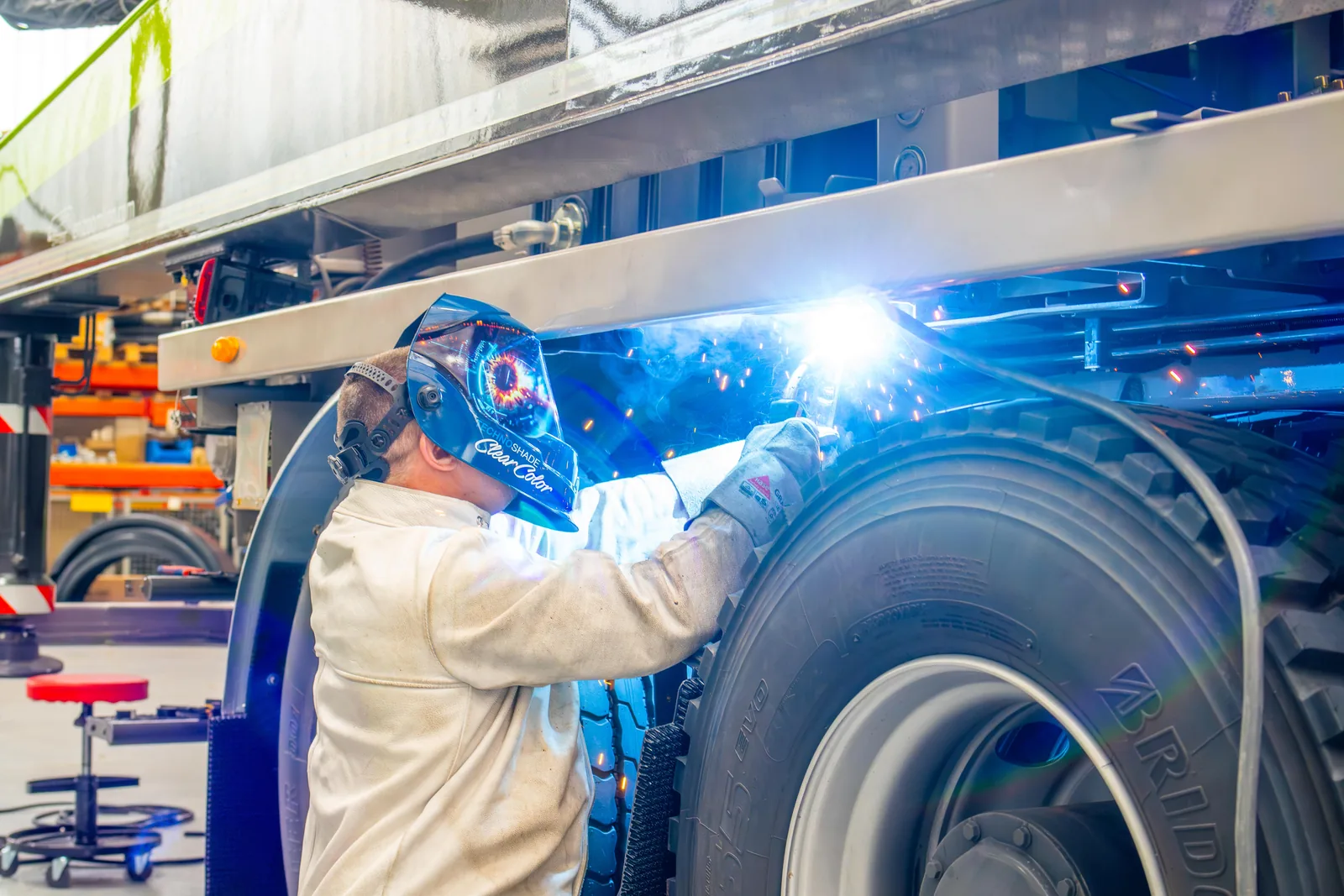Mitarbeiter der REMMEL AG schweißt kniend an einem Lkw, blaues Schweißlicht in der Werkstatt