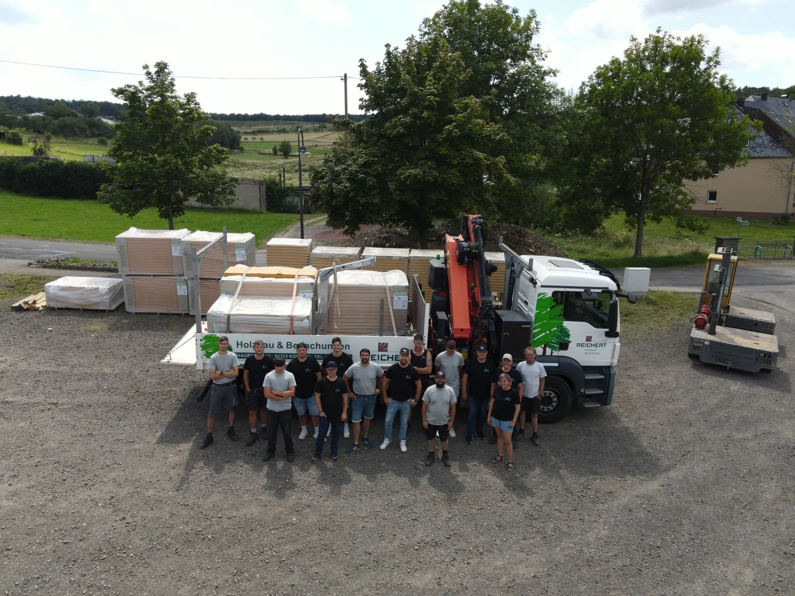 Drohnenaufnahme: Team von Reichert Holzbau steht vor einem beladenen Lkw mit Kran auf dem Firmengelände