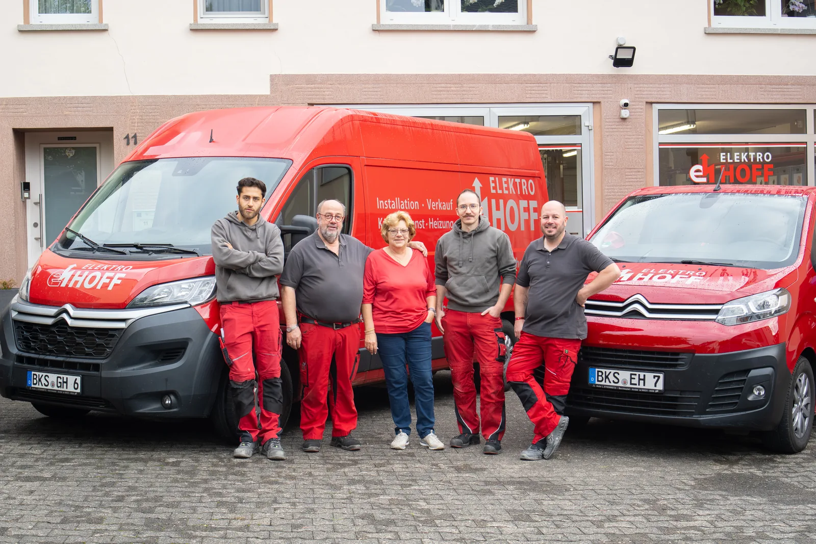 Team von Elektro Hoff steht vor zwei roten Firmenwagen am Betrieb