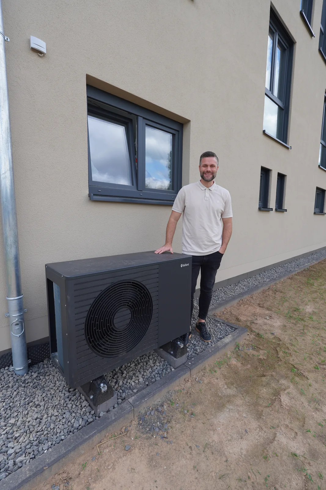 Ansprechpartner der Simon Kirst GmbH steht lächelnd neben einer neu aufgestellten Wärmepumpe an einem Neubau
